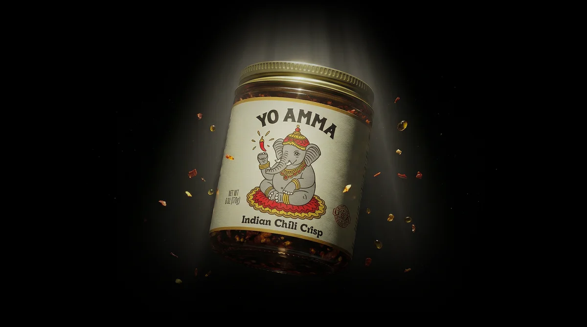 YoAmma Indian Chili Crisp jar lit by a spotlight with chili flakes floating around it